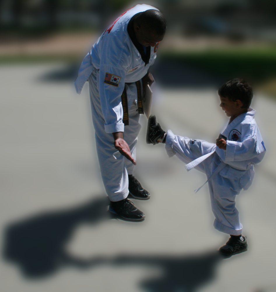 A young student practicing a front kick toward Master William's hand